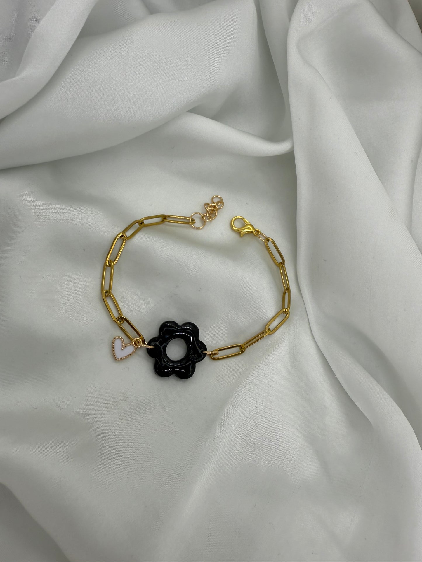 Bracelet doré, maille rectangle d'une largeur de 4 mm avec motif fleur 6 pétales de couleur noir d'environ 2,5 cm  et un charm cœur blanc entouré de doré. 